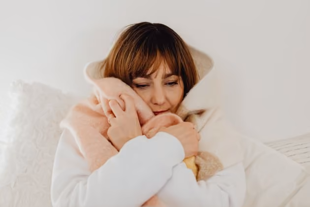 Woman wrapped in cozy soft blankets sitting against a white wall and cushions.